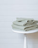 Sage green linen-cotton duvet cover set folded on bed with matching pillowcases