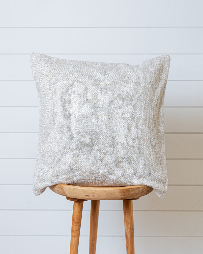 Beige textured cotton cushion cover on wooden stool against white wall