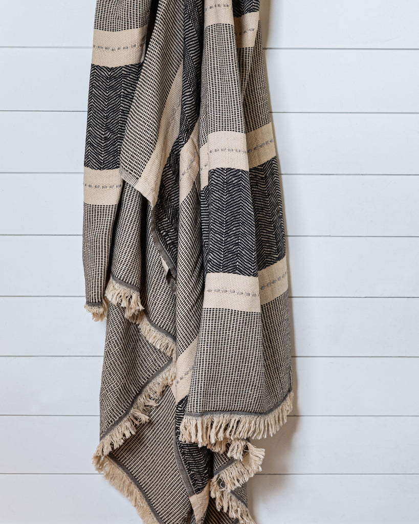 Black and sand cotton throw with grey accent hanging on white wall