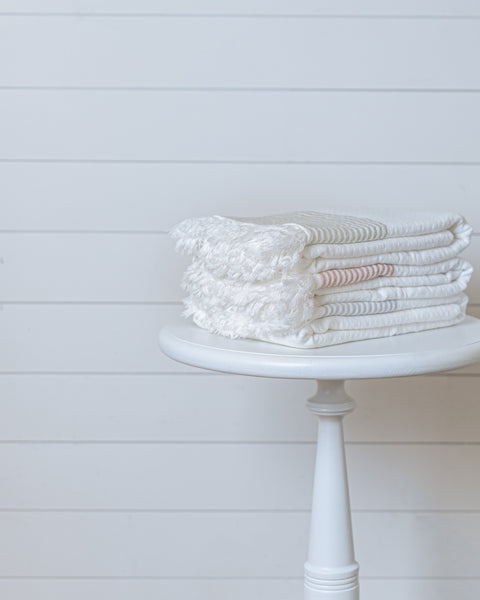 Stack of ivory Turkish cotton waffle bath towels with soft stripes on white stool