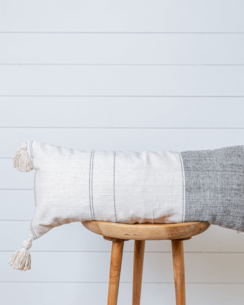 Rectangular cushion cover in natural linen and pearl grey with tassels on wooden stool
