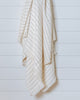 Ivory bamboo-cotton throw with fine grey stripes hanging on white wall