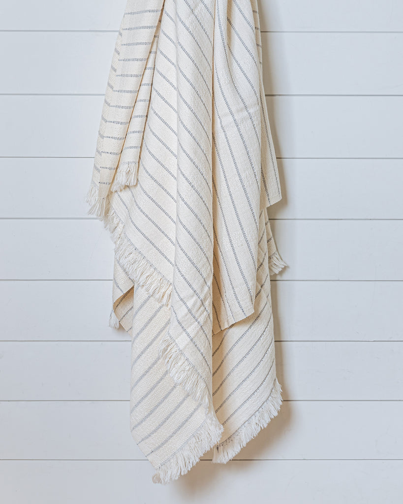 Ivory bamboo-cotton throw with fine grey stripes hanging on white wall