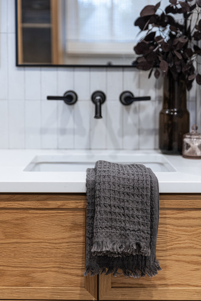 Taupe waffle-knit cotton hand towel draped over bathroom sink with wood cabinet